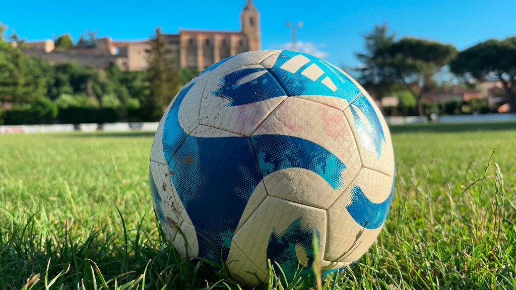 Balón de fútbol en el campo municipal del Arlanza, con la Colegiata de San Pedro de Lerma al fondo